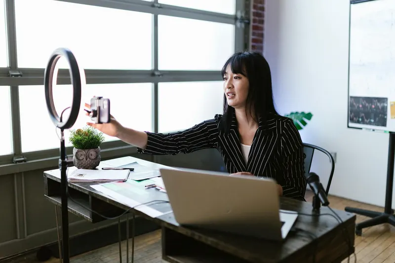 Woman using smartphone and ring light in office for content creation.